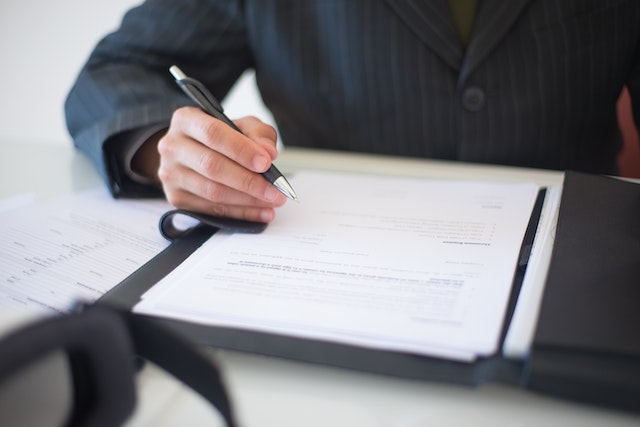 person in a suit holding a pen to sign a document in front of them